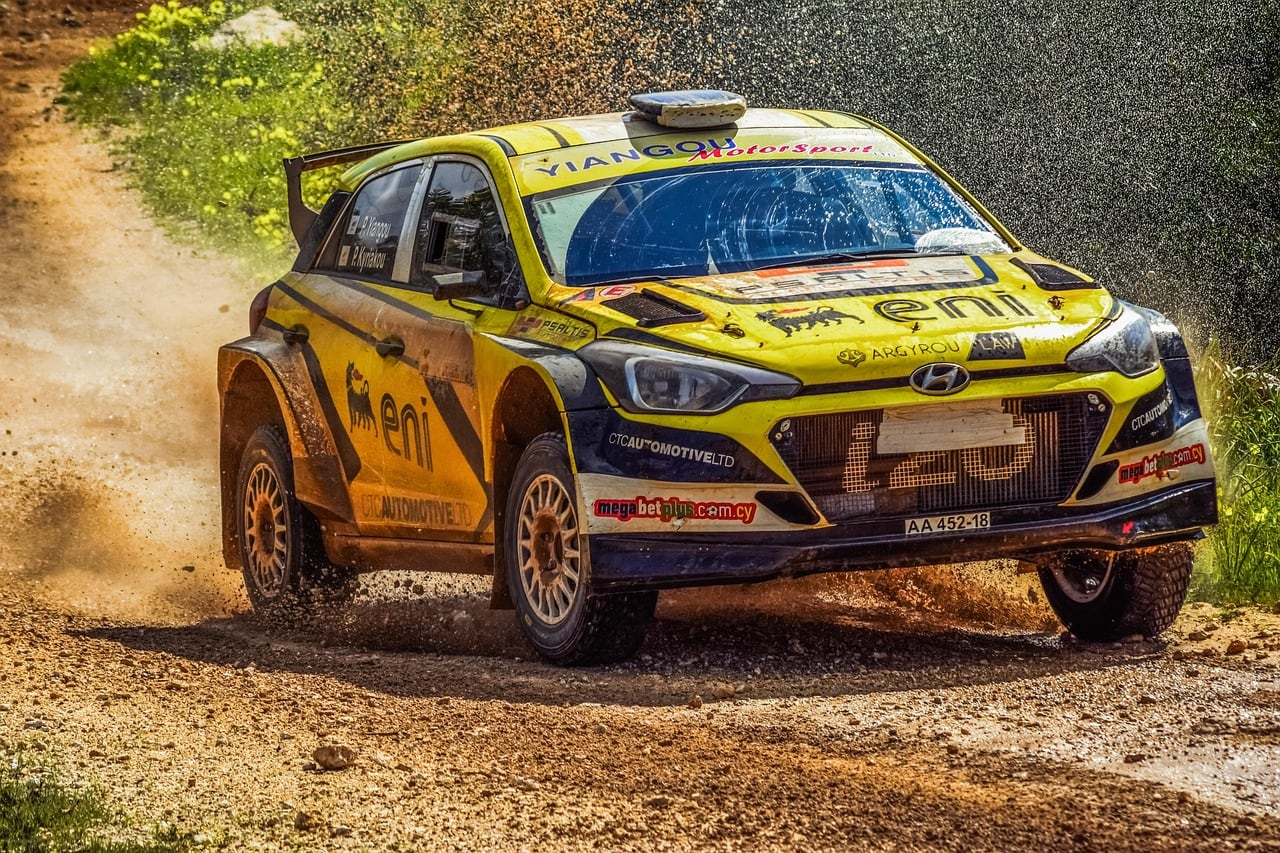 Auto da rally gialla e nera con loghi Eni che sfreccia su una strada sterrata, sollevando terra e polvere ai lati del percorso.