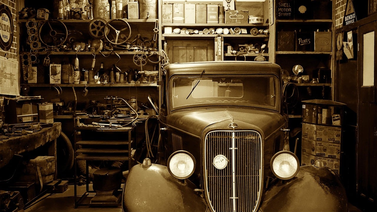Auto d'epoca in una vecchia officina in tonalità seppia, circondata da scaffali con attrezzi, volanti e latte d'olio.